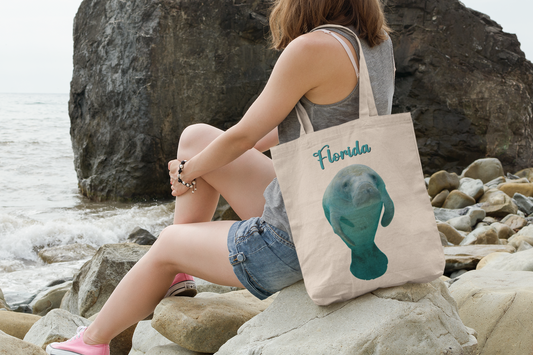 Florida Manatee Tote Bag, model with tote sitting on rock by ocean