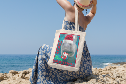 Merry Christmas Manatee Tote Bag, model sitting on beach overlooking ocean