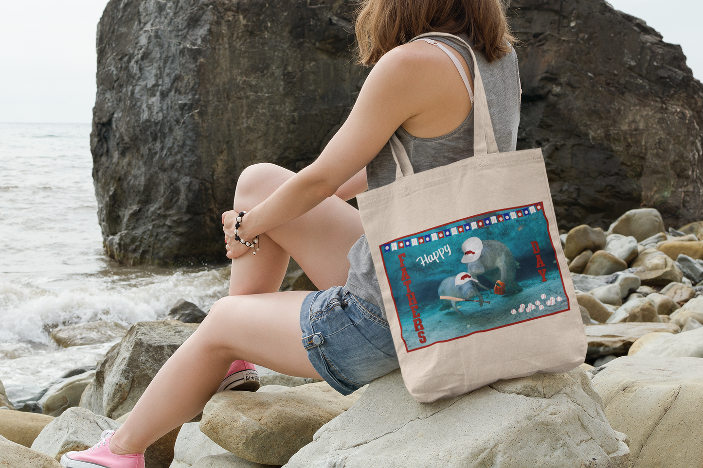 Happy Father's Day Manatee Tote Bag, model sitting on rocks by ocean