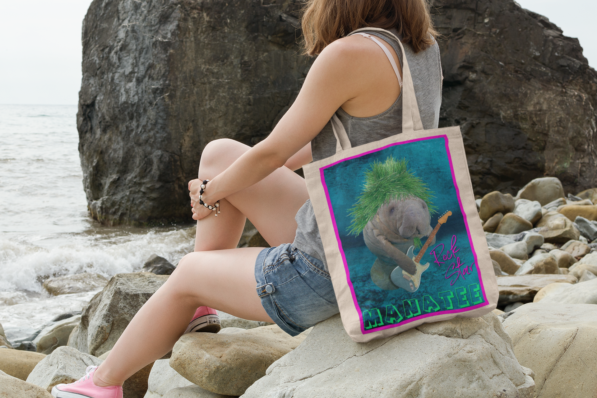 Rock Star Manatee Tote Bag, model sitting on rocks by ocean