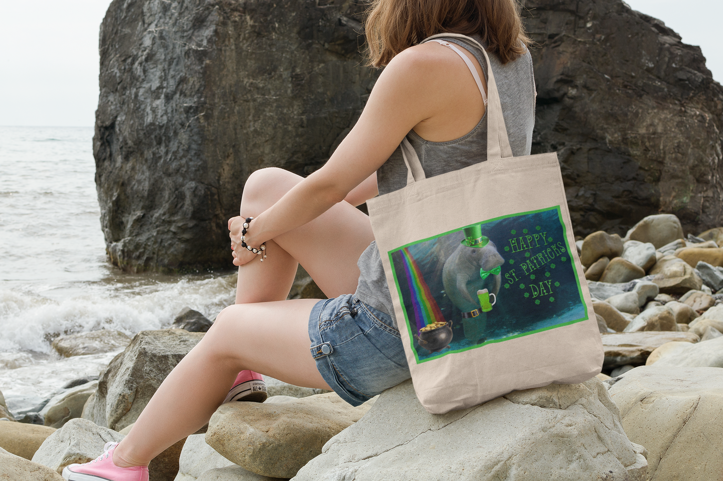 Happy St. Patrick's Day Manatee Tote Bag, model sitting on rocks by ocean