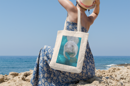 Cute Manatee Tote Bag, model with tote sitting on beach overlooking ocean