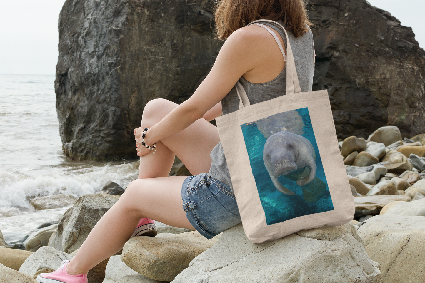 Cute Manatee Tote Bag, model with tote sitting on rocks by ocean