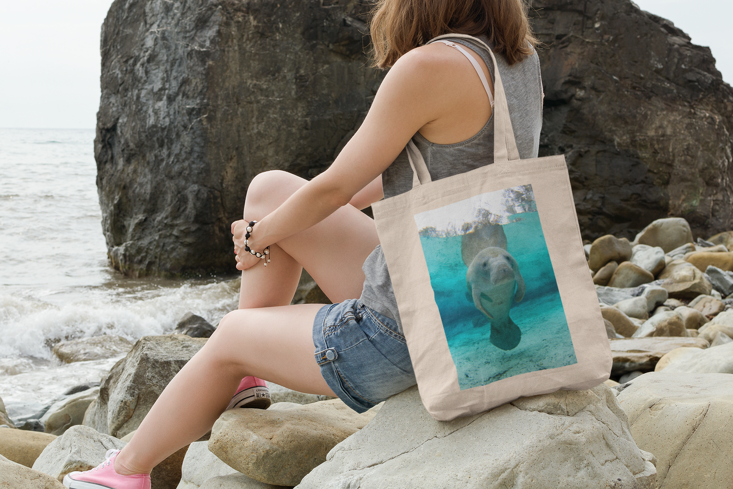 Adorable Manatee Tote Bag, model with tote sitting on rocks by ocean
