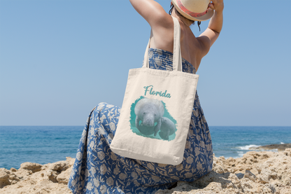 Manatee and Calf Feeding Tote Bag, model with tote sitting on beach overlooking ocean