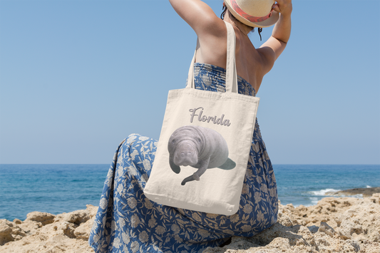 Manatee and Little Fish Tote Bag, model with tote sitting on beach overlooking ocean 