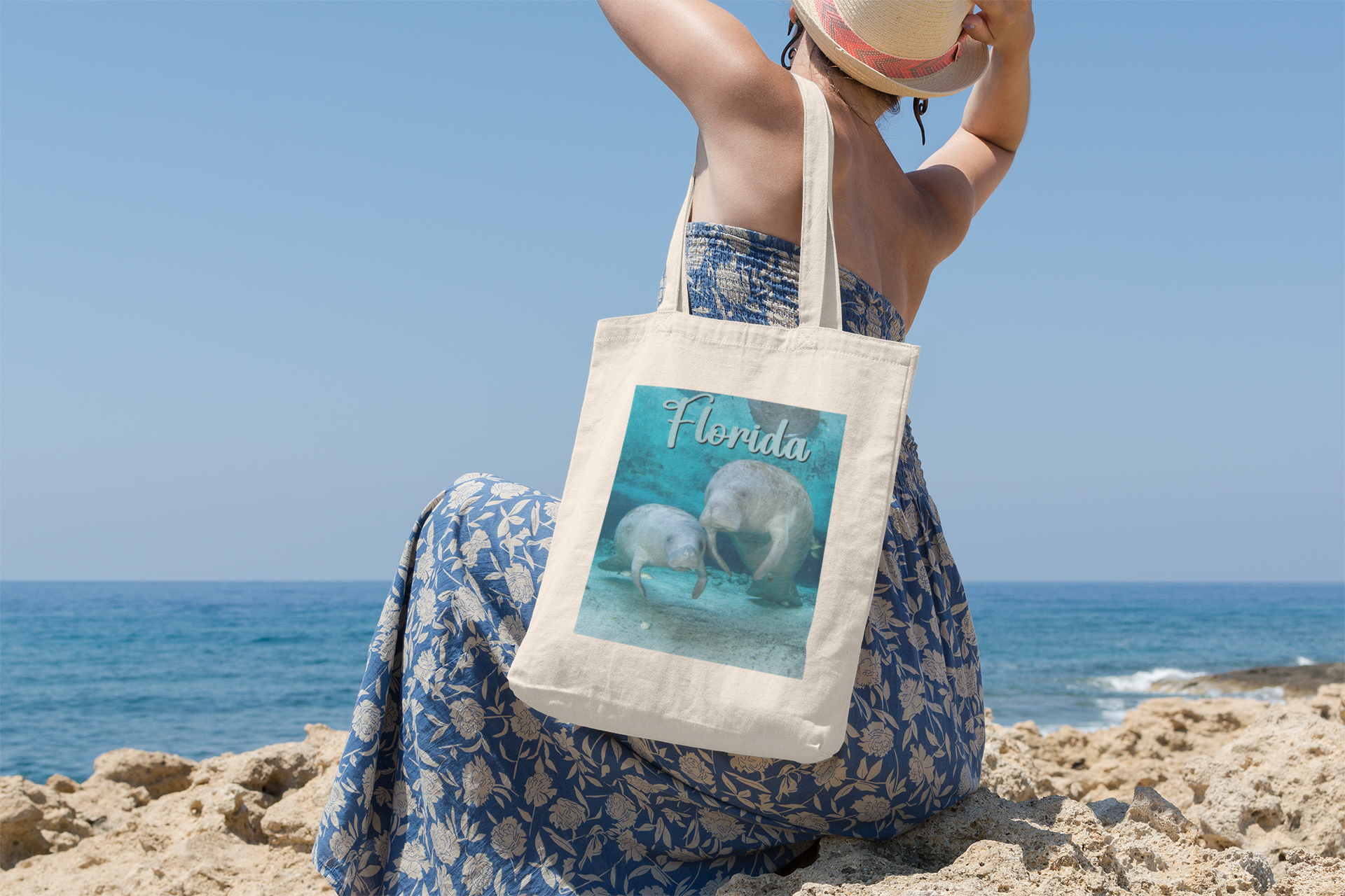 2 Graceful Manatees Tote Bag, model with tote sitting on beach overlooking ocean