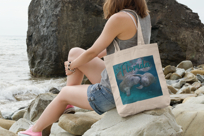 Playful Manatee Tote Bag, model with tote sitting on rocks by ocean